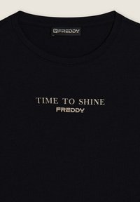 Camiseta negra de algodón con cuello redondo, con las palabras "TIME TO SHINE" y "FREDDY" impresas en texto beige claro en el centro. Textura suave.