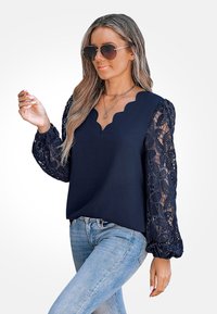 Navy blouse with scalloped neckline and long lace sleeves. Paired with light wash denim. Features a relaxed fit and textured lace detail.