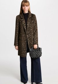 Cappotto a stampa leopardata con colletto sagomato, camicia nera, jeans a gamba larga e borsa nera strutturata con manico.