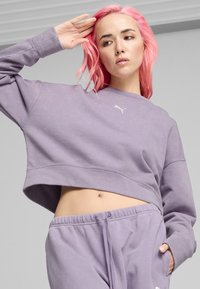 Sudadera morada recortada en tejido suave con un ajuste relajado, que presenta un pequeño logotipo blanco y detalles acanalados en el dobladillo y los puños.