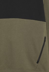 Crewneck sweatshirt i olivgrön och svart, med en texturerad tyg, en horisontell färgblockdesign och en ficka med dragkedja.