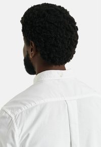 Weißes Hemd mit Button-Down-Kragen, mit einer Rückenfalte und dezenten Nähdetails, von hinten gezeigt, um die Stofftextur zu betonen.