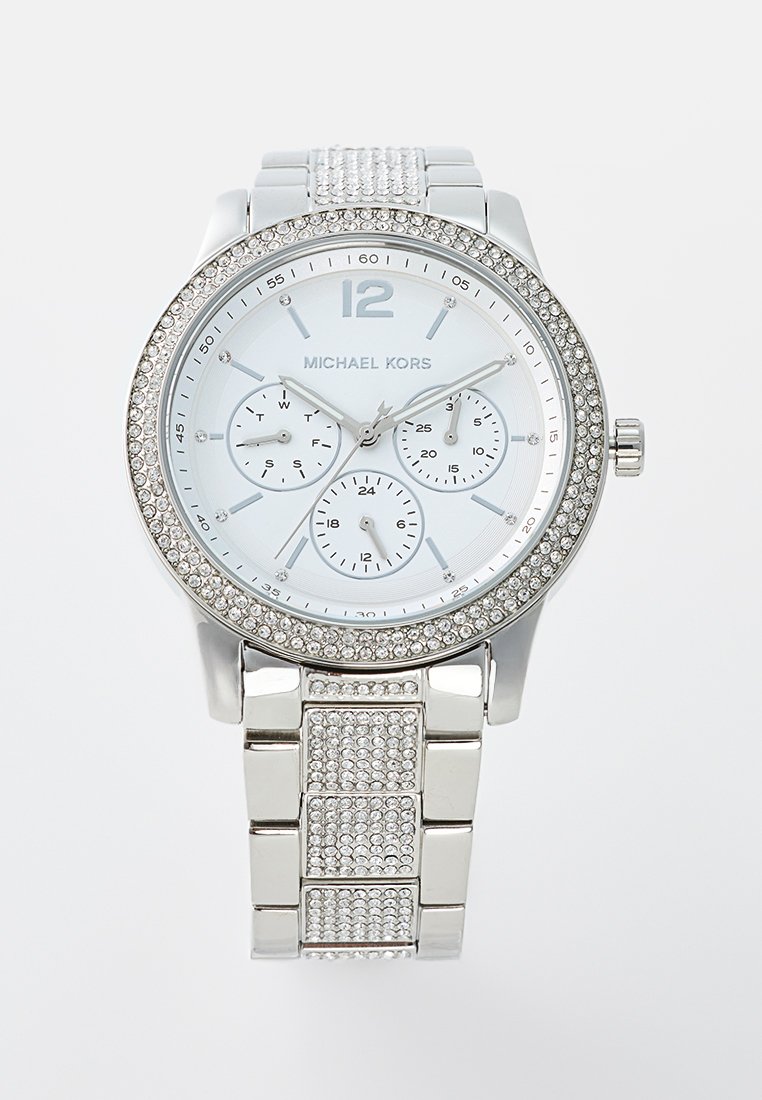 Montre argentée avec un cadran rond, un cadran blanc, trois sous-cadrans et des embellissements en cristal sur la lunette et le bracelet. Elle comprend un bracelet à motif.