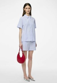 Ensemble comprenant un haut à manches courtes rayé bleu clair et blanc, ainsi qu'un short, accompagné d'un sac à main rouge et de chaussures à bout pointu argentées.