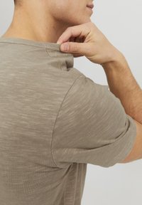 Lys brun, kortærmet t-shirt med et struktureret, let ribbet stof. Viser detaljer om krave og skuldre, tætsiddende silhuet.