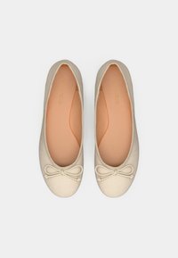 Ballerines beiges avec une texture côtelée, bout rond et un petit nœud décoratif à l'avant. Semelle intérieure rose pâle avec le nom de la marque embossé.
