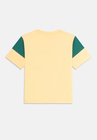 T-shirt à manches courtes en coton jaune pâle, avec des accents verts sur l'épaule. Design classique à col rond. Texture lisse, coupe décontractée.