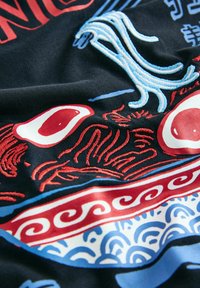 Zwarte stof met levendige geborduurde patronen in rood, wit en blauw, waaronder gestileerde golven en abstracte vormen.