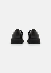 Zwarte leren schoenen met een gladde afwerking, lage hak en ronde neus. De achterkant toont een strak ontwerp met subtiele stiksels.