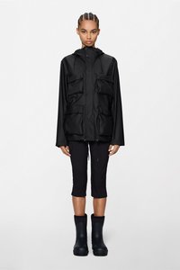 Μαύρο αδιάβροχο μπουφάν με κουκούλα, δύο τσέπες στο στήθος και ρυθμιζόμενο κορδόνι στο στρίφωμα, σε συνδυασμό με μαύρο cropped παντελόνι και μαύρες μπότες.