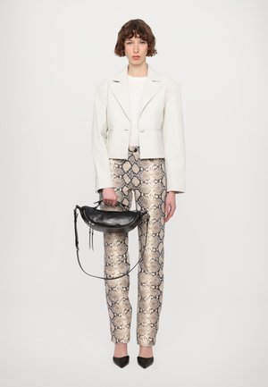 Veste blanche courte, top crème, pantalon en imprimé serpent beige et marron, sac à main noir avec sangle, chaussures noires à bout pointu, fond neutre.