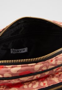 Interno di una borsa in tessuto rosa con zip dorata e fodera nera. Presenta un'etichetta con la scritta "DAY ET". Texture liscia con motivi colorati.