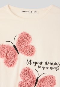 Biała bawełniana koszulka z dwoma różowymi, teksturowanymi motylami oraz czarnymi konturami, z napisem "niech twoje marzenia będą twoimi skrzydłami" poniżej.