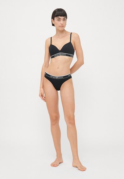 Zwart lingeriesetje bestaande uit een gepadded bh met een diepe V-hals en een bijpassende string, beide met gebrandmerkte elastische banden. Gladde textuur en aangesloten ontwerp.