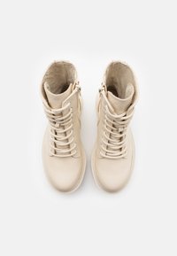 Bottines en cuir beige avec fermeture à lacets, bout rond et intérieur texturé. Fermetures éclair latérales et détails de design minimalistes.