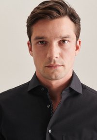 Zwarte overhemd met knoopsluiting, slim fit, zachte textuur en subtiele blauwe details bij de kraag. Bevat een keurig gestikt zakje en knopen.