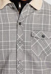 Rutig skjorta i svart och vitt. Har en mjuk, beige sherpa-krage, knappstängning och en bröstficka med knapp. Strukturerad tyg.