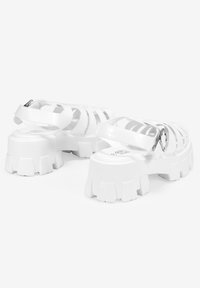 Sandalias gruesas blancas con un diseño de múltiples correas, material de plástico suave, suela de goma gruesa y un detalle de hebilla lateral.