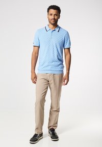 Světle modrá pletená polo košile s texturovaným vzorem, kontrastním límečkem, béžové kalhoty a černé tenisky s bílými akcenty.