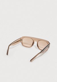 Καφέ διαφανή γυαλιά ηλίου με τετράγωνα φακούς και κομψούς βραχίονες, με ελαφρύ καφετί αποχρωματισμό και ελάχιστες λεπτομέρειες εξαρτημάτων.