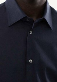 Camicia blu navy con colletto classico. Presenta una texture liscia e due bottoni visibili sulla pattina. Dettagli di design semplici e sartoriali.