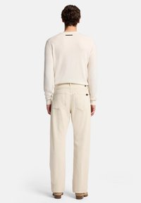 Maglione a maniche lunghe color crema chiaro con scollo rotondo e un piccolo accent black sul retro, abbinato a pantaloni beige chiaro dall' fitting morbido.