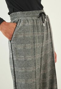 Schwarz-weiße karierte Hosen mit elastischem Bund und Kordelzug, mit seitlichen Taschen und lockerem Schnitt. Texturiertes Stoffdesign.
