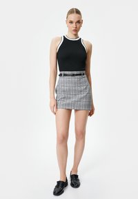 Schwarzes geripptes Tanktop mit weißen Akzenten, kombiniert mit einem grauen karierten Minirock mit einem schwarzen Gürtel und flachen schwarzen Schuhen.