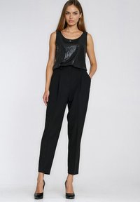 Czarny top na ramiączkach z cekinami, zestawiony z czarnymi, zwężanymi spodniami z wysokim stanem. Modelka nosi czarne, spiczaste szpilki. Prosty, elegancki design.