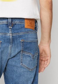 Vaqueros vaqueros en azul claro con un acabado texturizado, que cuentan con un parche de cuero con el logo y dos bolsillos traseros con costuras en contraste.