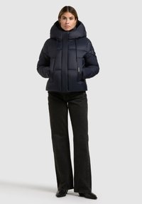 Donsjack in donker marineblauw met een hoge kraag, capuchon, rits aan de voorkant en zijzakken. Gladde textuur met een quilted patroon en trekkoorden.