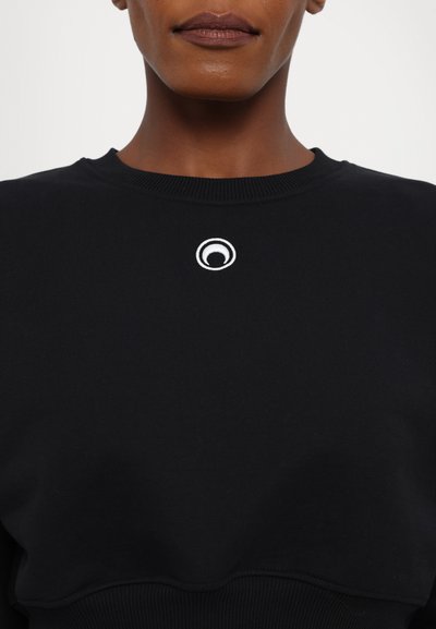 Black sweatshirt featuring a round neckline and a small embroidered white logo at the chest. The fabric has a smooth, textured finish.