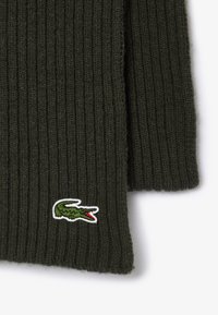 Maglione lavorato a maglia verde scuro con texture a coste e logo del coccodrillo Lacoste in dettagli bianchi e rossi sul lato sinistro in basso.