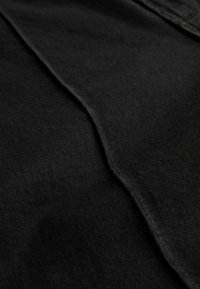 Približni prikaz slojeva crne tkanine s vidljivim šavovima i teksturom, naglašavajući preklapajuće rubove i detalje šavova.