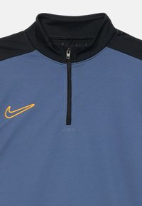 Pulover albastru cu fermoar și accente negre, dotat cu guler înalt și logo portocaliu Nike. Textură netedă și design minimalist.