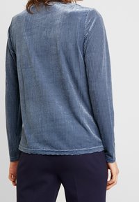 Langärmliges blaues Oberteil mit einem strukturierten, gitterartigen Muster. Der Stoff wirkt leicht und hat eine glatte Oberfläche, mit einem runden Ausschnitt und geradem Saum.