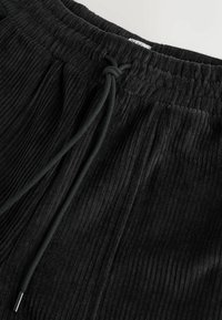 Sorte joggers med ribbet tekstur, der har en elastisk talje og justerbar snor. Blødt materiale og afslappet pasform for komfort.