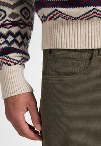 Suéter de punto con base color crema y patrón geométrico multicolor. Pantalones de pana oliva con un acabado texturizado acanalado y detalle de bolsillo lateral.