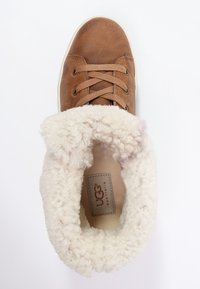 Baskets en cuir marron avec un col en fourrure crème duveteuse, bout rond et lacets marron. Logo UGG visible à l'intérieur.