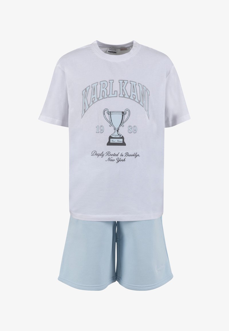 Άσπρο κοντομάνικο T-shirt με γραφικό τρόπαιο, κείμενο «"KARL KANI 1989"» και ανοιχτό μπλε σορτς.