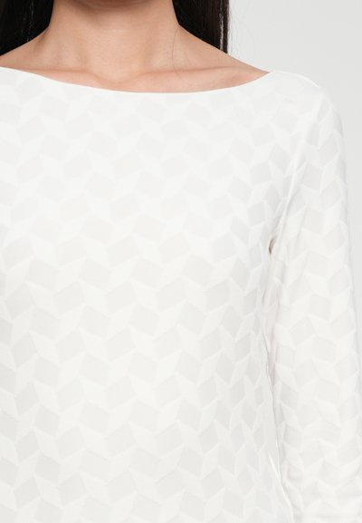 Hvit langermet topp med et teksturert geometrisk mønster, med bred båtnek og glatt stoff.