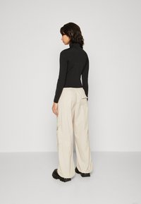 Svart langermet rullekrage genser kombinert med beige cargo bukser. Antrekket har en avslappet passform, med lett, teksturert stoff og sidelommer.