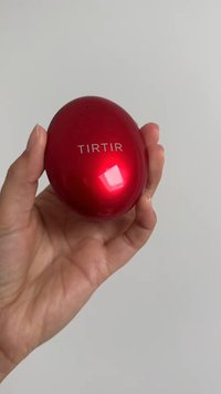 Rød, ovalformet beholder med en blank finish, med ordet "TIRTIR" i hvid. Holdt i en hånd mod en ensfarvet baggrund.