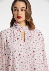 Lys pink bluse med blomster mønster, nøglerumsudskæring og samling ved halsen. Lavet af et blødt, gennemsigtigt stof med en svajende silhuet.