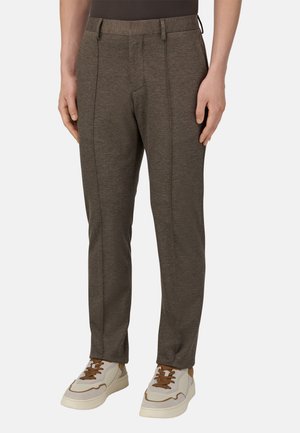 Grau, maßgeschneiderte Hose aus einem strukturierten Stoff, mit einem glatten Bund und vorderen Bügelfalten, kombiniert mit weißen und braunen Sneakers.