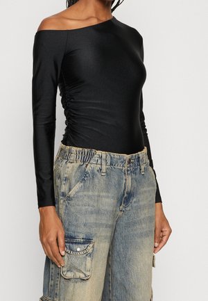 Body lungo nero off-shoulder con maniche lunghe, caratterizzato da dettagli arricciati sul lato. Abbinato a pantaloni cargo in denim blu sbiadito e larghi.
