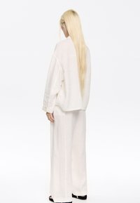 White linen oversized shirt and matching wide-leg pants. Smooth texture, simple design, visible stitching, and buttons on shirt cuffs.