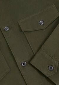 Olivgrünes Cordhemd mit zwei Brusttaschen, schwarzen Knopfverschlüssen und strukturiertem Stoff. Verfügt über einen klassischen Kragen und lange Ärmel.