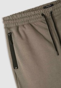 Szare spodnie dresowe z elastycznym paskiem, sznurkiem oraz bocznymi kieszeniami na zamek. Materiał jest gładki o lekko fakturowanej powierzchni.