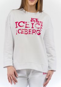 Felpa grigia chiara con lettering rosa audace e irregolare che riporta la scritta "ICEBERG." Presenta una vestibilità rilassata e maniche lunghe. Texture liscia.